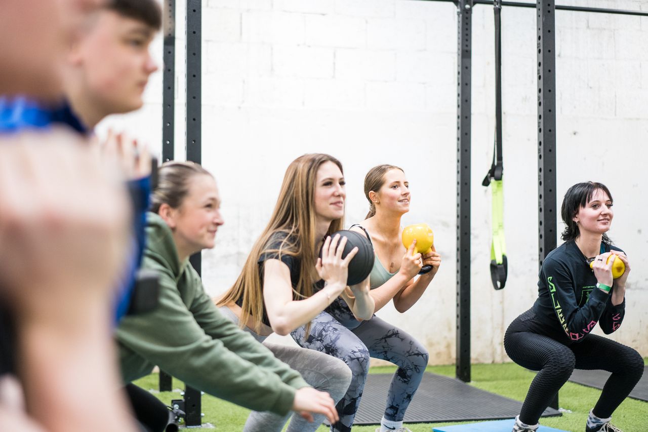 Group of students in the gym doing squats with a kettlebell