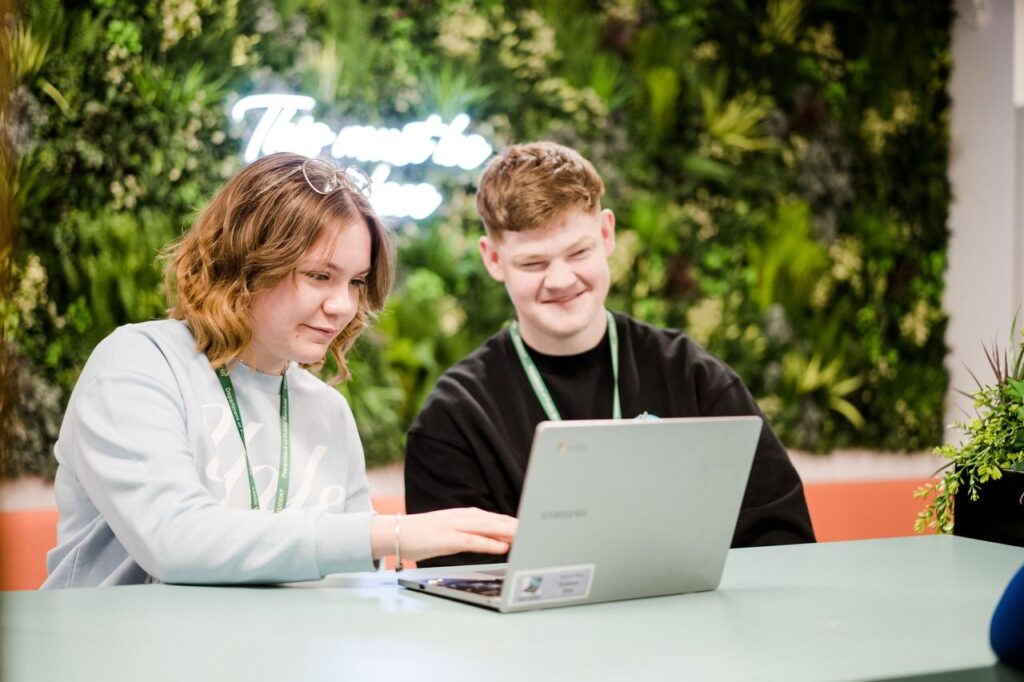 Two students sat down working on the same laptop together