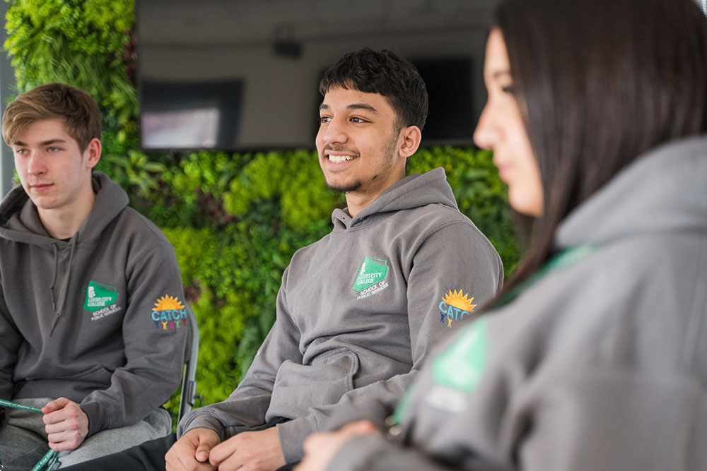 Three Leeds City College Public Service students sat down smiling wearing CATCH hoodies