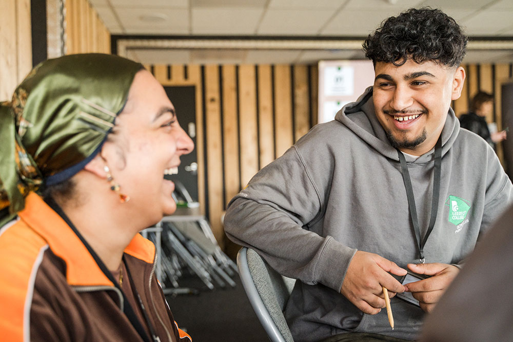 Public Services CATCH student sat in classroom laughing with member staff sat next to him