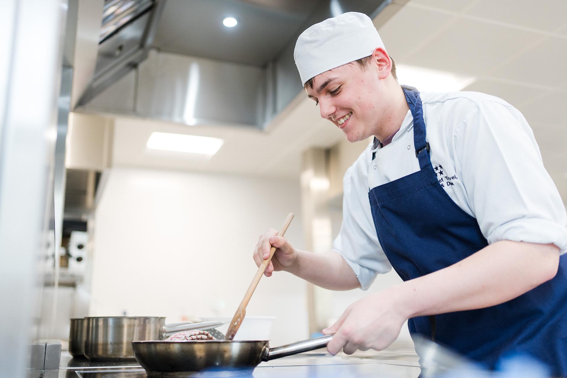 Talented culinary student in chef hat and apron cooking in the kitchen smiling
