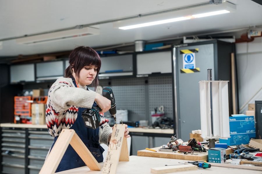 Theatre design student using a drill connecting a wooden frame together for a production stage