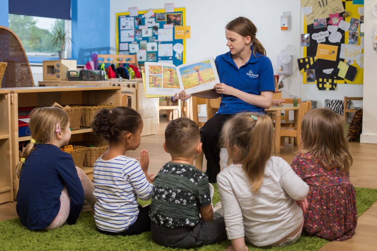 Early years student reading a children's book to a group of young children