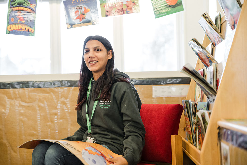 Person sat in the Education and Early Years room next to children's books with a book on knee
