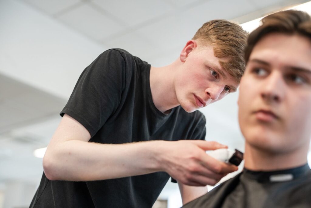 Barber student using a hair clipper to work on a clients hair