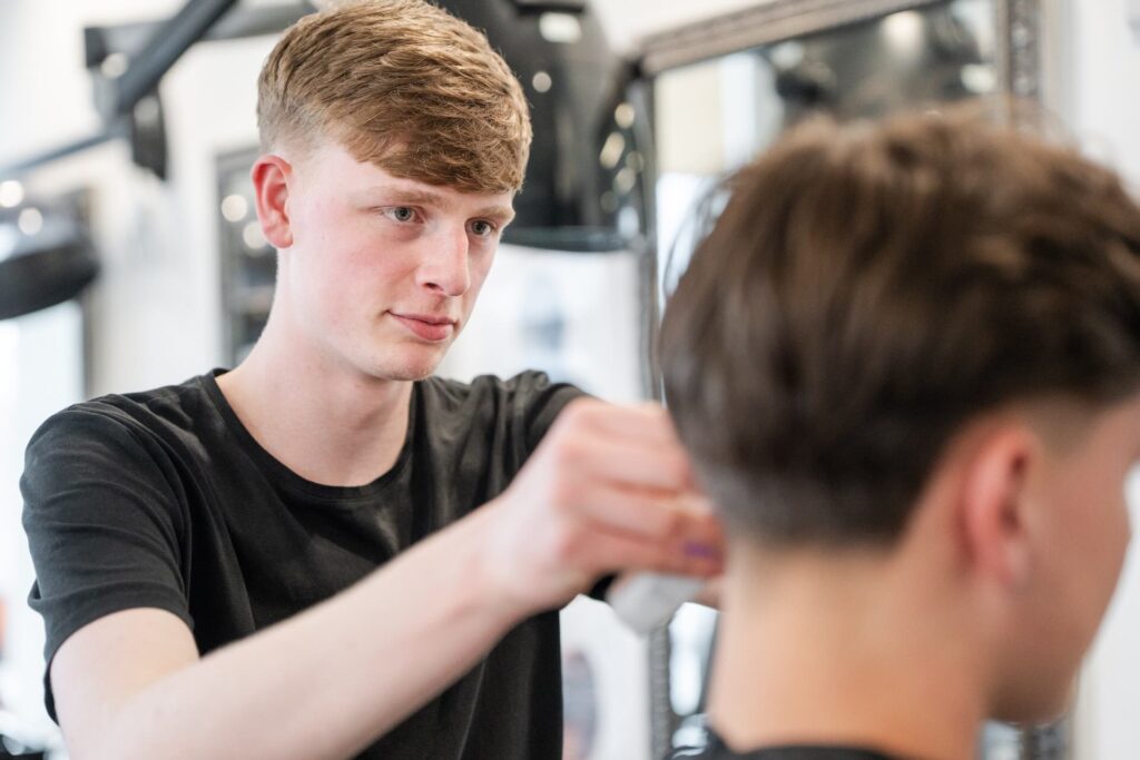 Barber student using a hair clipper to work on a clients hair
