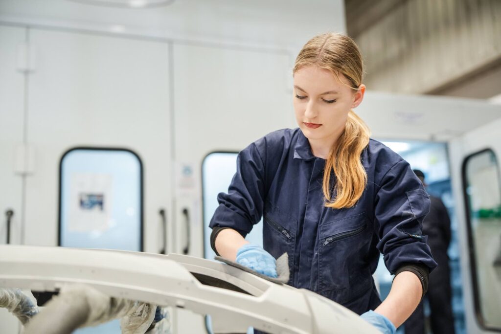 Female Motor Vehicle student sanding a car to prepare for a respray
