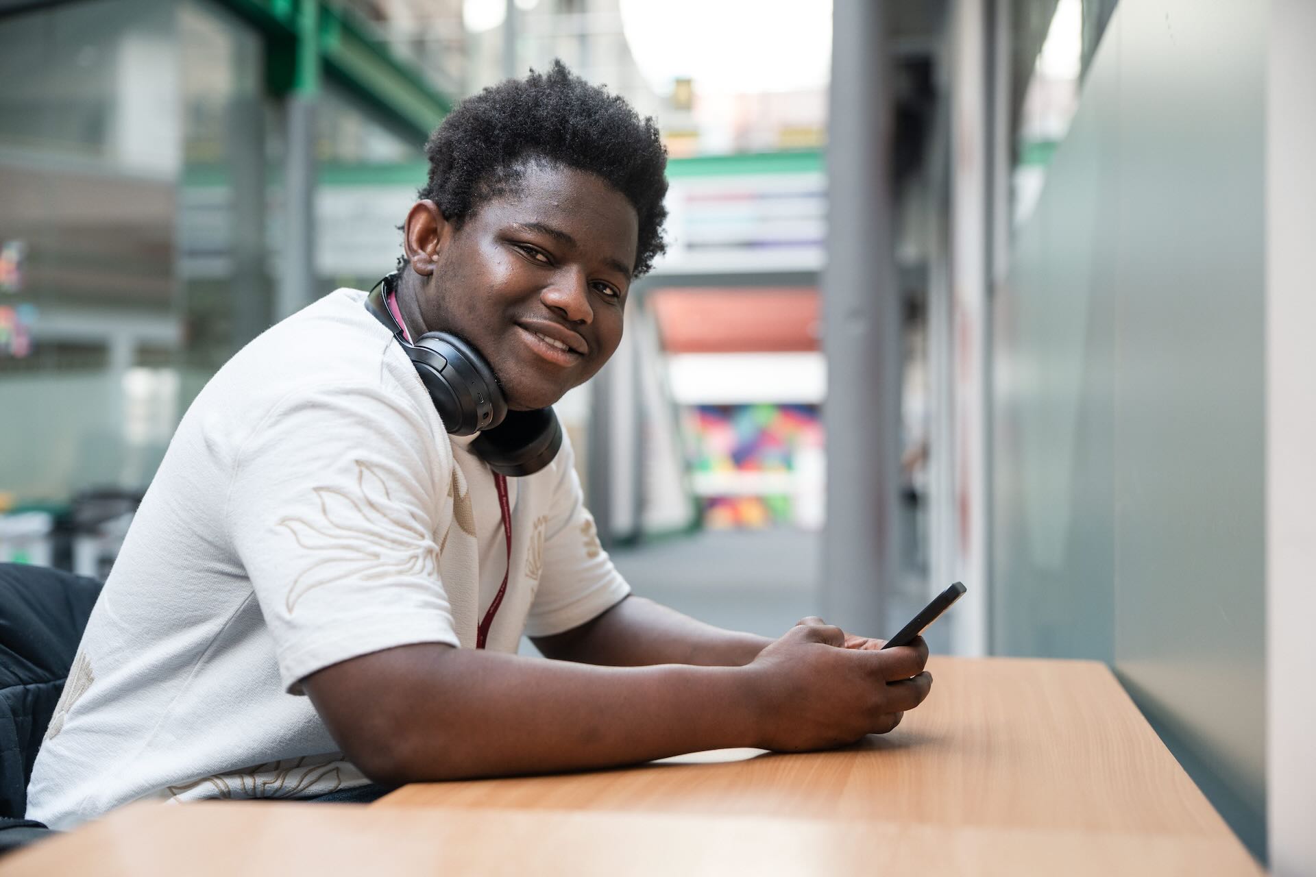 Student on the bottom floor of the red print hall in PrintWorks playing on his phone, smiling looking at the camera