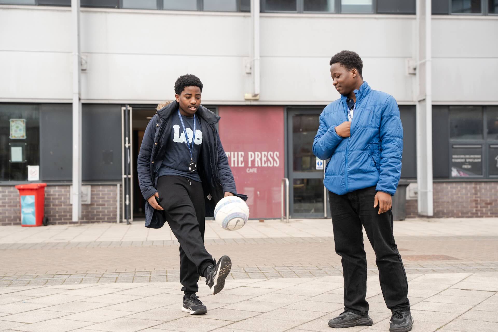 Two students in the courtyard of PrintWorks kicking a football to one another