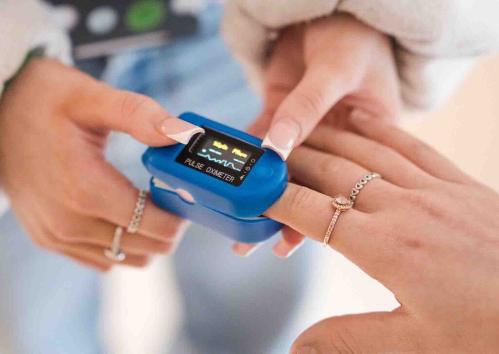 Close up of a blue digital pulse oximeter attached to a person's index finger with the digital display screen active