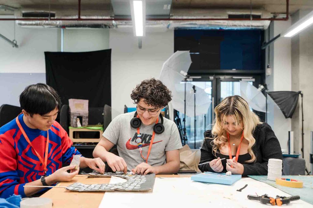 Students happily settle into their seats in the studio, collaborating and crafting prototypes for their projects