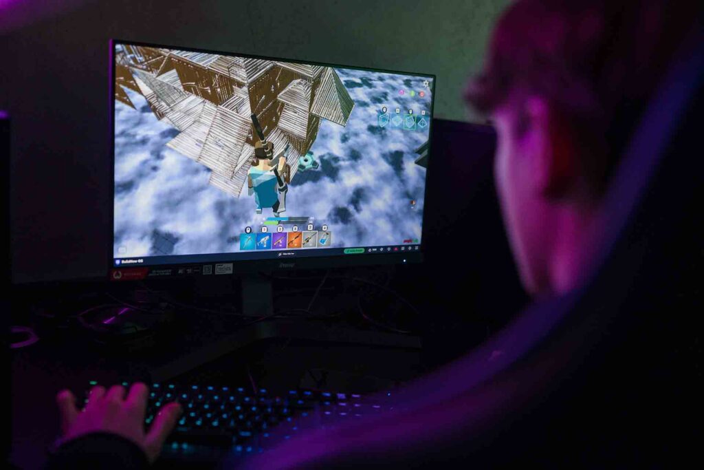 A student is seated in a dark-themed classroom, focused on the computer, which shows vibrant animated graphics