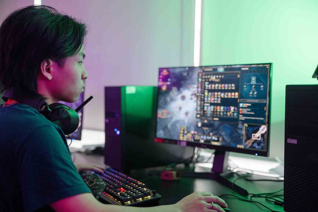 In a dimly lit classroom, a student with headphones hanging around his neck sitting in front of a computer, engaged with vibrant animations displayed on the screen
