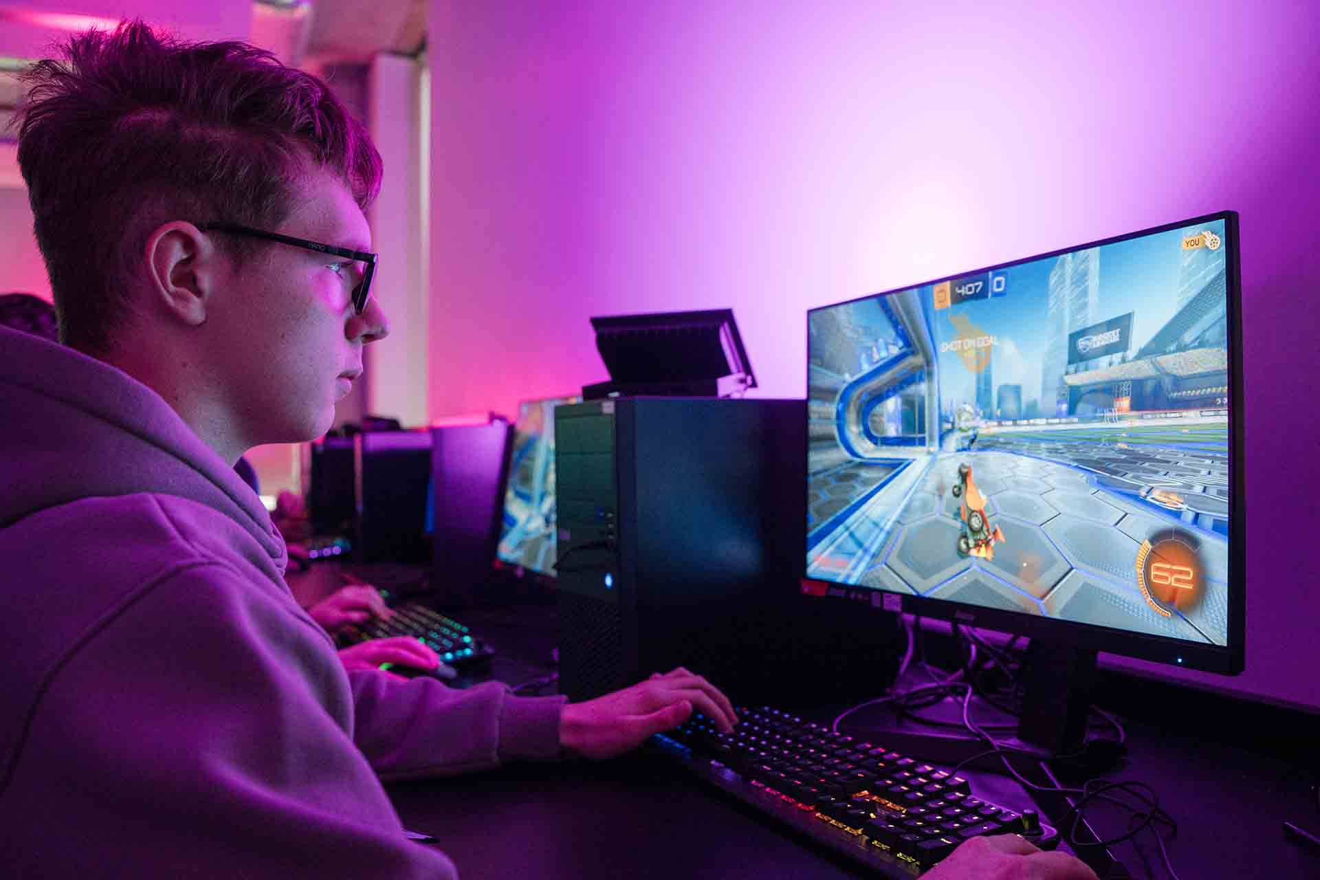 In a softly lit classroom, student wearing a hoodie sitting in front of a computer, captivated by the colourful animations flashing on the screen