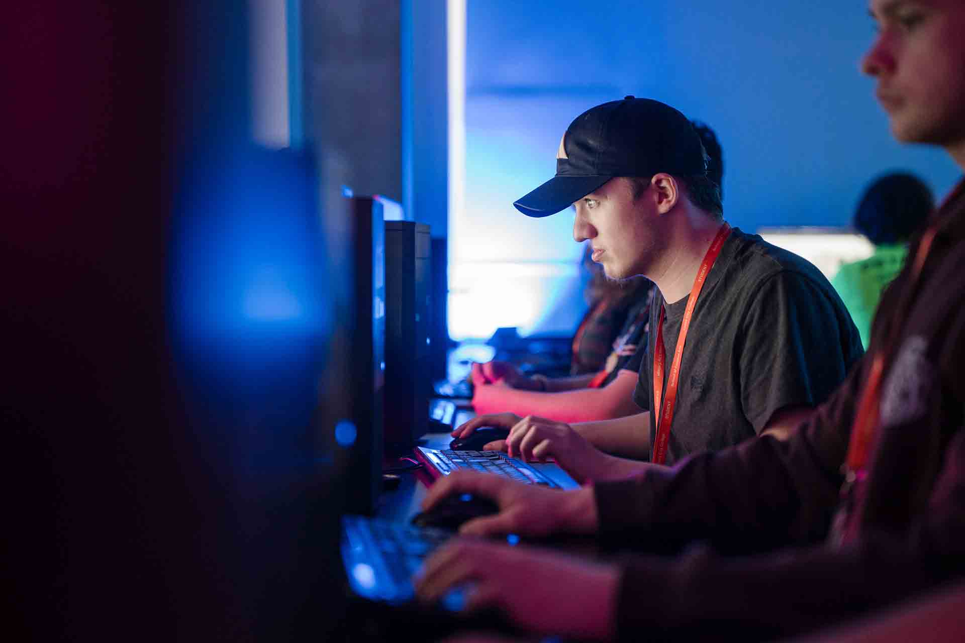 Students sitting in a dimly lit classroom, with one student in a baseball cap concentrating on the screen