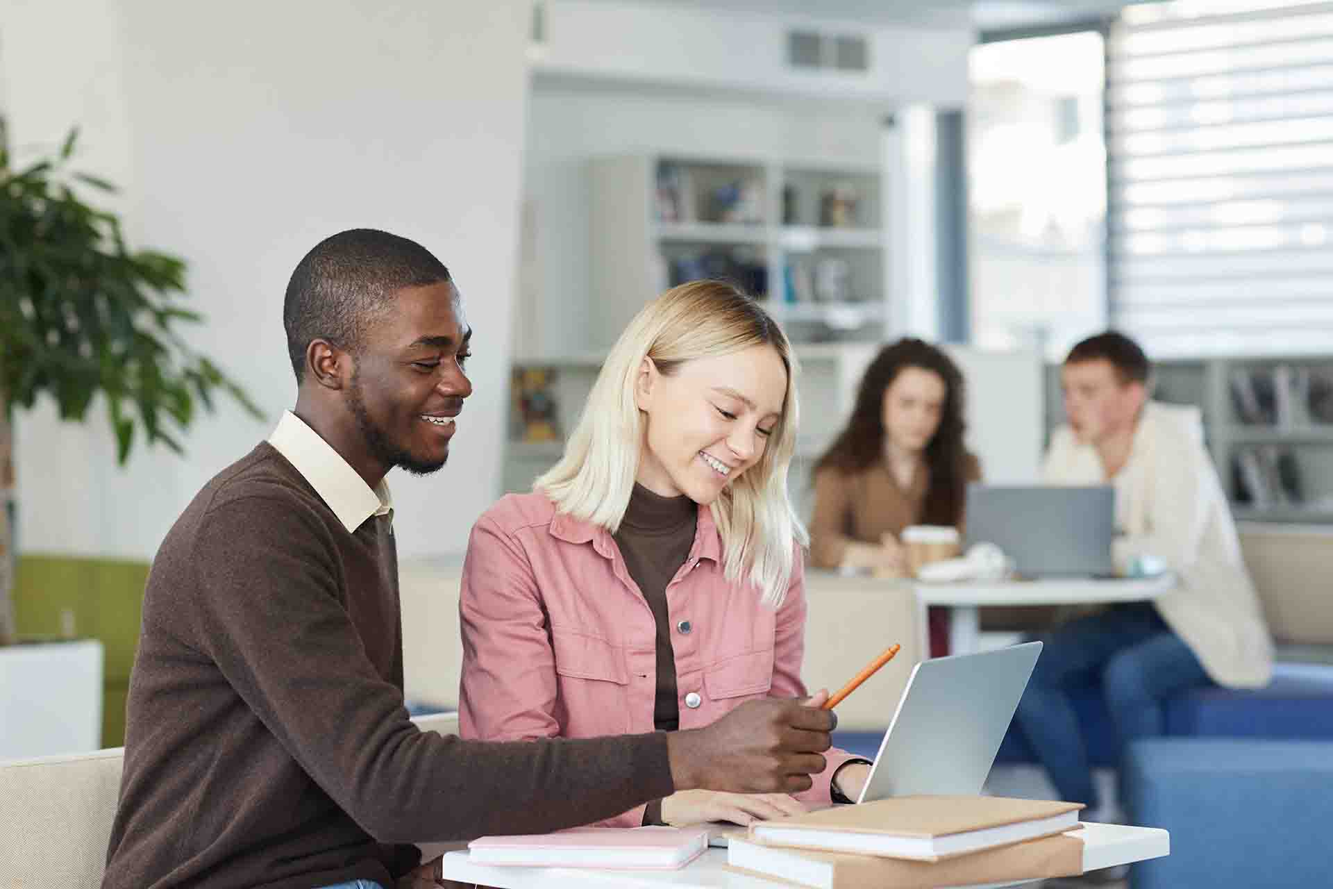 Two students smiling while studying together at a laptop