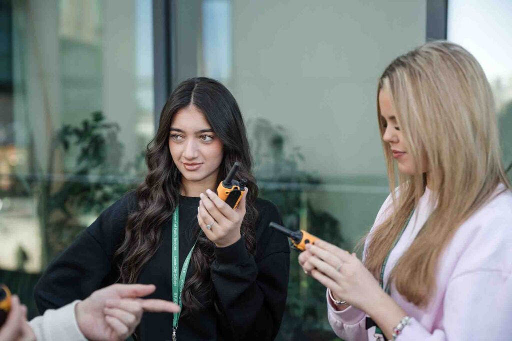 Two female Leeds City College Public Services students holding yellow and black walkie-talkies while engaged in a practical group training exercise.