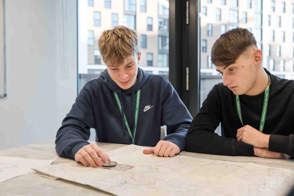 Two male Public Services students sitting at a desk together, using a compass and map to practice navigation skills.