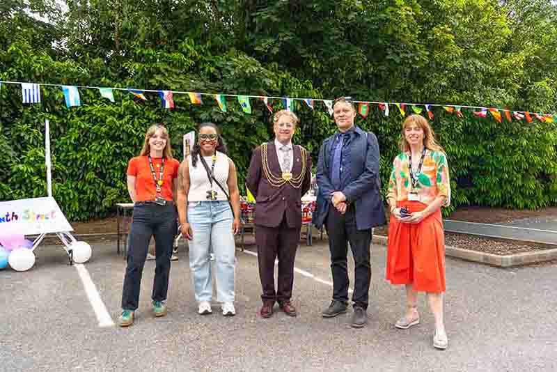 Five people, including a local mayor wearing a ceremonial chain, standing together outdoors under bunting flags