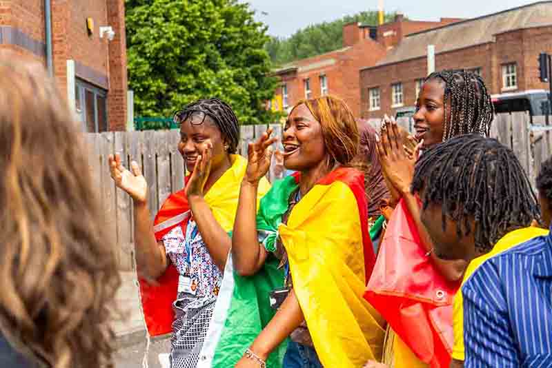 Joyful students draped in colourful flags clapping and cheering together outdoors