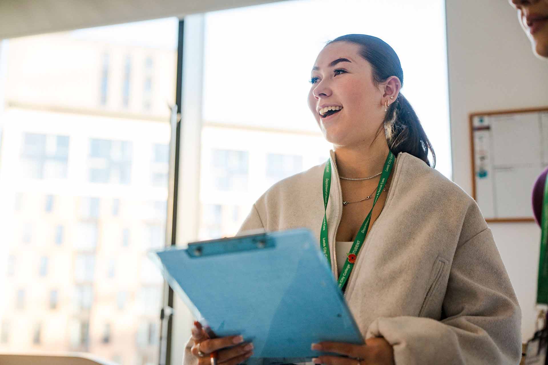 A smiling Leeds City College student wearing a green lanyard and holding a blue clipboard.