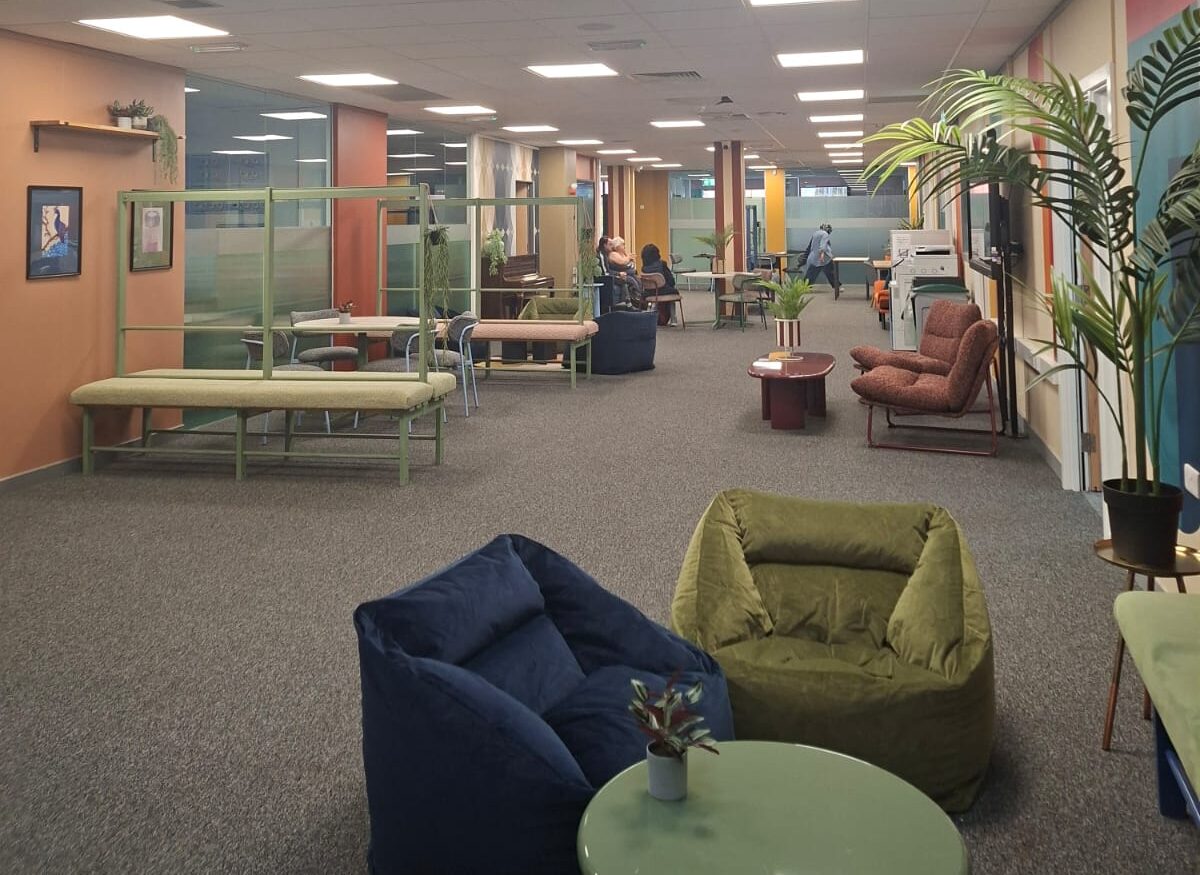 Spacious open-plan lounge and office common area with varied seating and indoor plants.