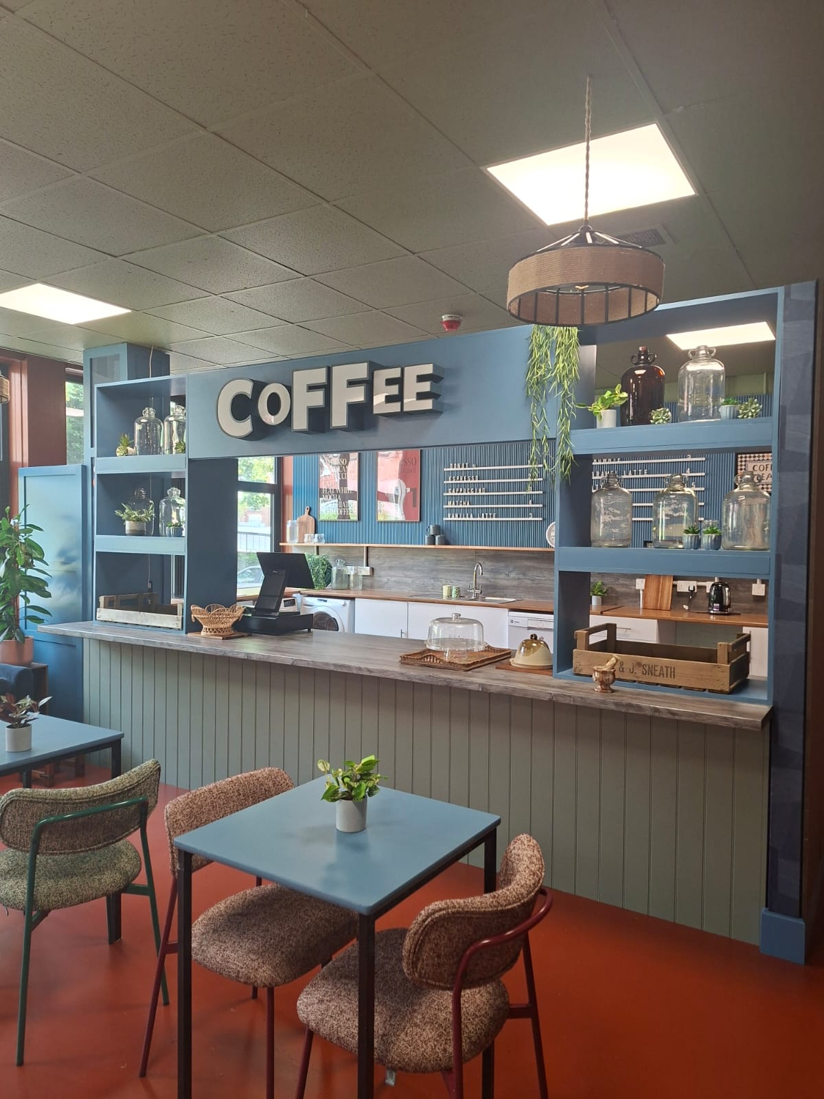 Cafe service counter with large wooden COFFEE sign and foreground dining seating.