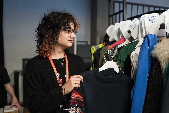 A person is looking at a clothes rail full of outfits, selecting one coat hanger with black clothes on it