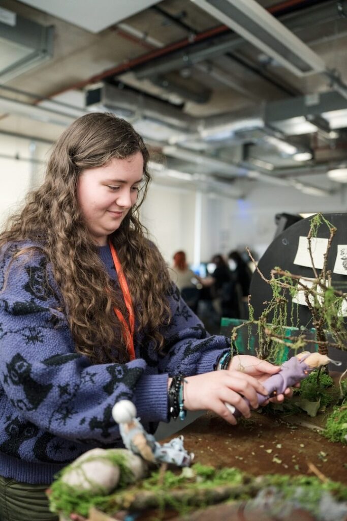 Student making a claymation with two figures on a miniature woodland scene