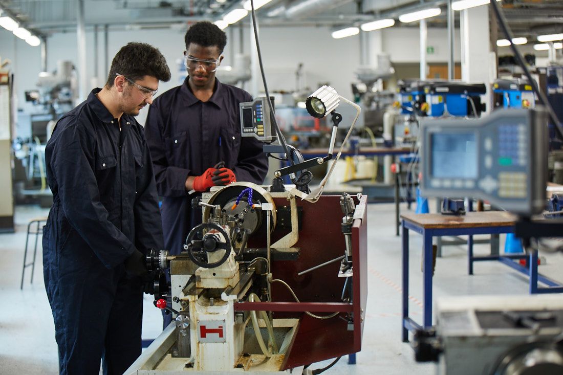 Two engineering students in overalls working on machinery